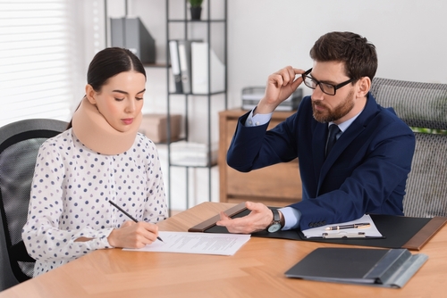 Distracted driving accident lawyer speaking with an injured female client wearing a neck brace during a legal consultation.