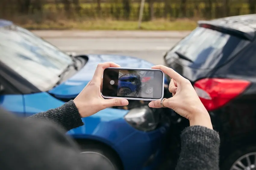 Person using smartphone to photograph car accident scene damage for personal injury claim evidence documentation