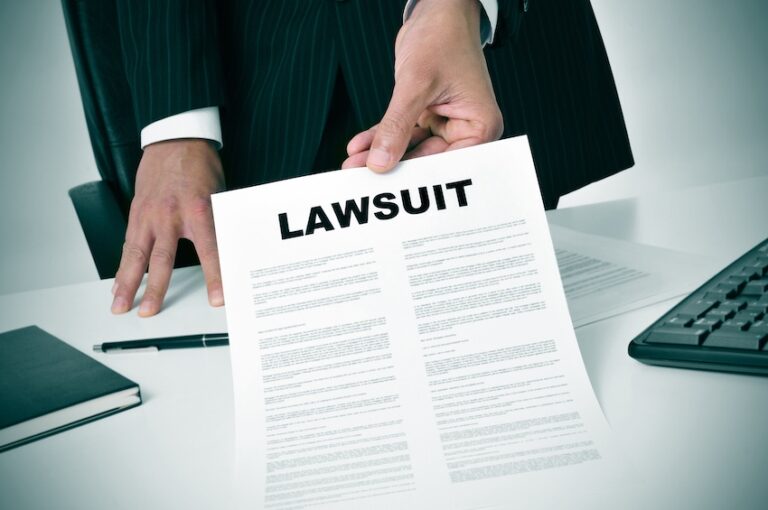 A person in a dark pinstripe suit sitting at a desk holds out a formal document with the word "Lawsuit" printed in bold at the top with a keyboard- notepad- and pen visible on the desk surface- illustrating the moment an attorney from Ross Moore Law presents a client with the filed paperwork for a personal injury lawsuit in Tennesse.