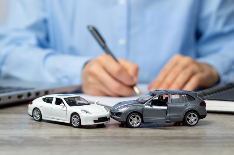 A person in a blue shirt writes on documents behind two toy cars positioned in a head-on collision on a desk- illustrating the paperwork and documentation required when filing a car accident lawsuit after a crash in Georgia.