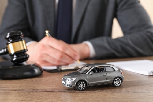 A car accident lawyer signing legal documents while at a desk near a toy car and a judge's gavel.