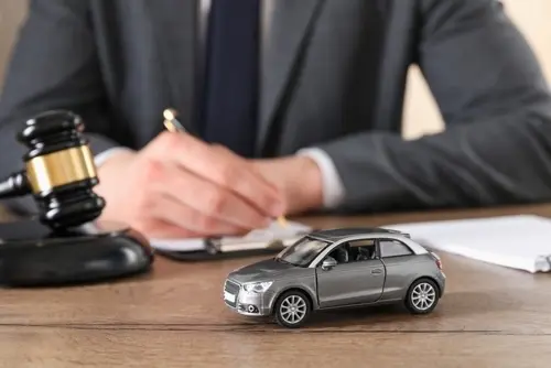 A car accident lawyer signing legal documents while at a desk near a toy car and a judge's gavel.