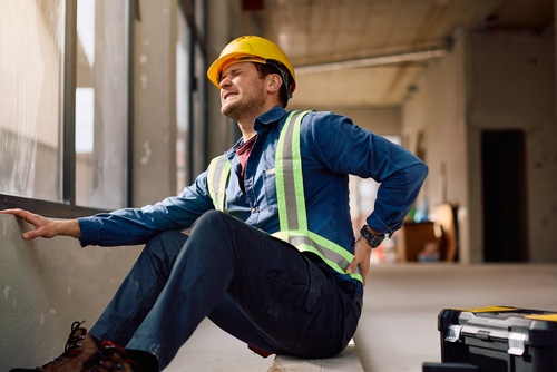 A man holding his back after injuring himself at a construction site and will now need a construction accident lawyer to help him with his claim.
