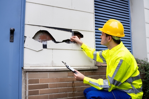 A man is inspecting the wall of a house due to property damage and the homeowner gathering information to contact a property damage lawyer.