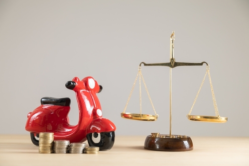 A toy motorbike near a judge's scale and coins to represent compensation a motorcycle accident lawyer can recover in a claim.