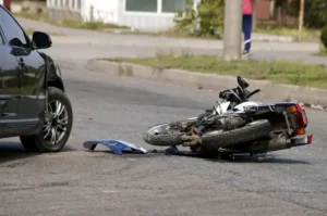 Motorcycle accident lawyer case showing a crashed motorcycle on the street near a vehicle with a pedestrian in the background.