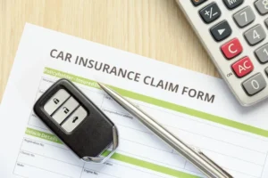 Car accident claim form with vehicle details, key fob, pen, and calculator for insurance documentation.