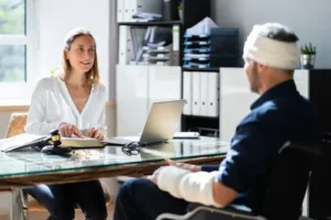 Injured motorcycle accident victim with bandaged head and arm consulting with an experienced motorcycle accident lawyer at a desk in a law office.