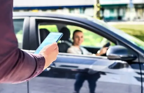 Johns Creek rideshare accident lawyer concept showing pedestrian with phone requesting ride while distracted driver approaches in vehicle.